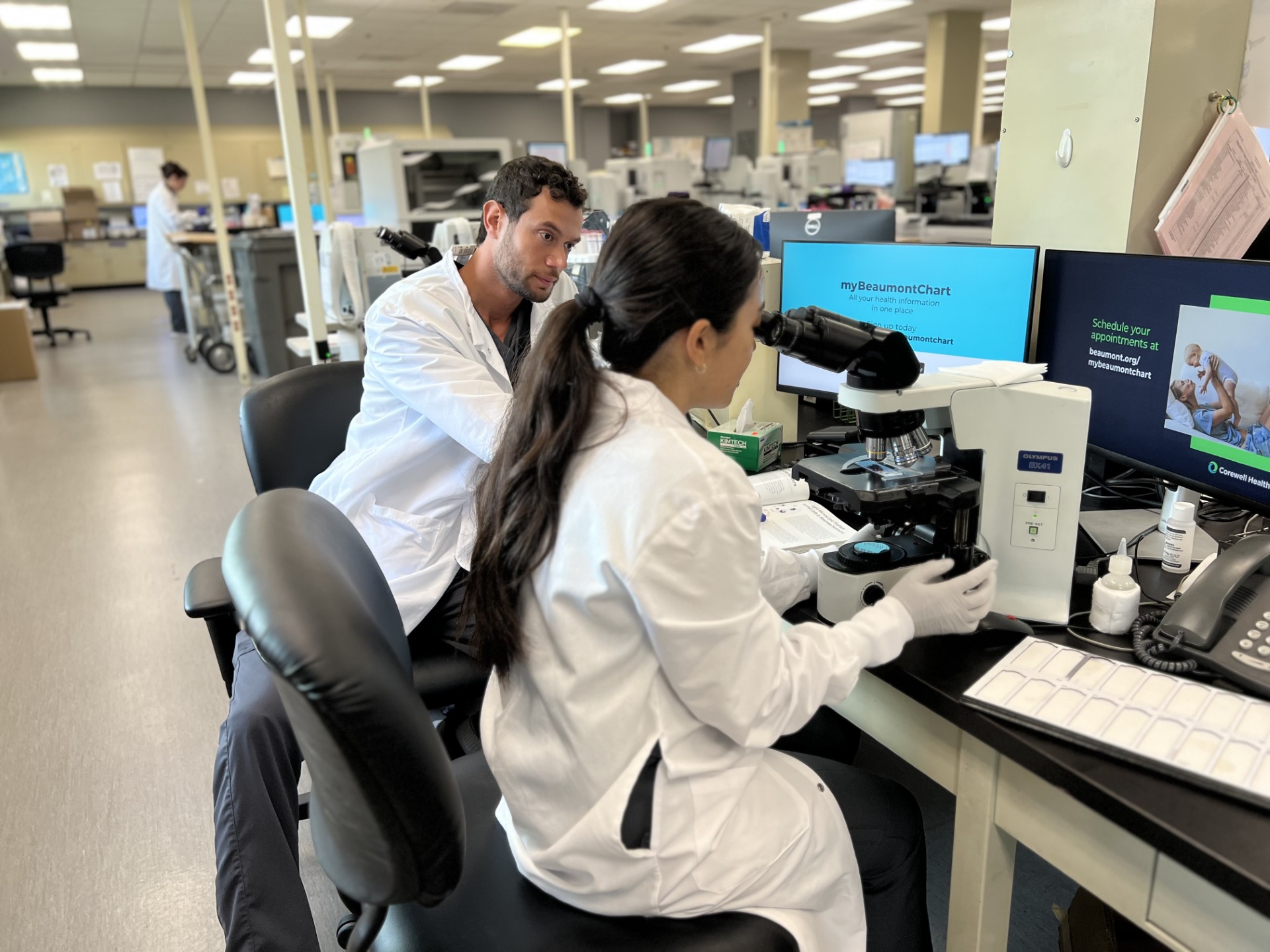two lab workers in white lab coats looking into microscope